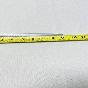 May include: A silver metal tool with a yellow measuring tape. The tape shows measurements in inches, with numbers from 3 to 11. The tool is on a white surface.