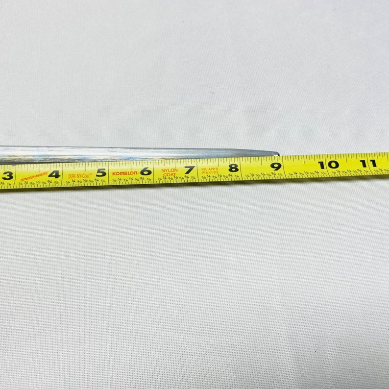 May include: A silver metal tool with a yellow measuring tape. The tape shows measurements in inches, with numbers from 3 to 11. The tool is on a white surface.
