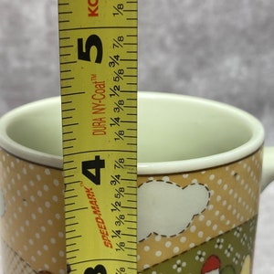 May include: A yellow and brown ceramic mug with a white cloud design and polka dots. The mug is 4 1/2 inches tall and has the words "Speed-Mark" and "Dura NY-Coat" printed on the side.