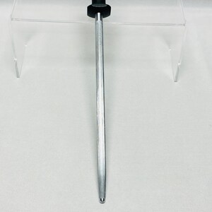 May include: A silver metal knife sharpener with a black handle. The sharpener has a long, tapered rod, designed for honing the edge of a knife. The handle is cylindrical and provides a secure grip. The sharpener is designed to maintain the sharpness of kitchen knives.