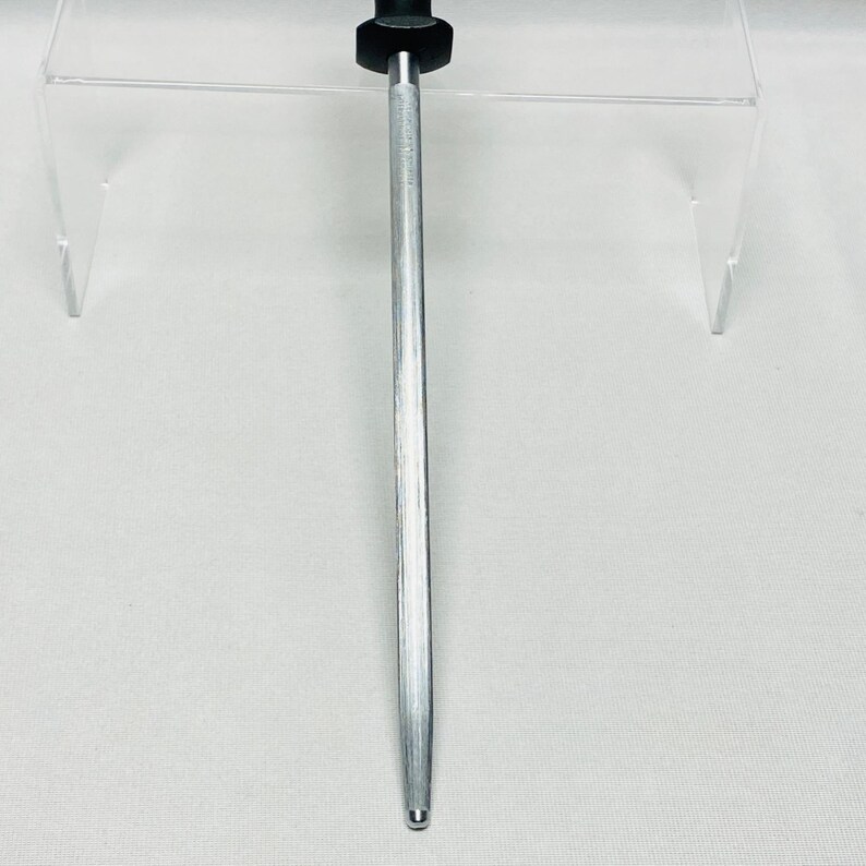May include: A silver metal knife sharpener with a black handle. The sharpener has a long, tapered rod, designed for honing the edge of a knife. The handle is cylindrical and provides a secure grip. The sharpener is designed to maintain the sharpness of kitchen knives.