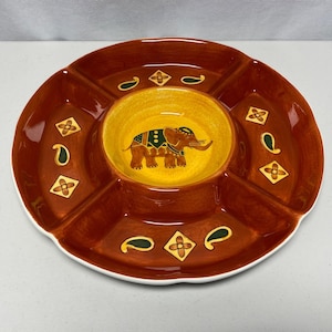 May include: A round, divided serving dish with a brown exterior and a yellow center. The center features an elephant design. The dish is decorated with paisley and floral patterns. The dish has a white rim.