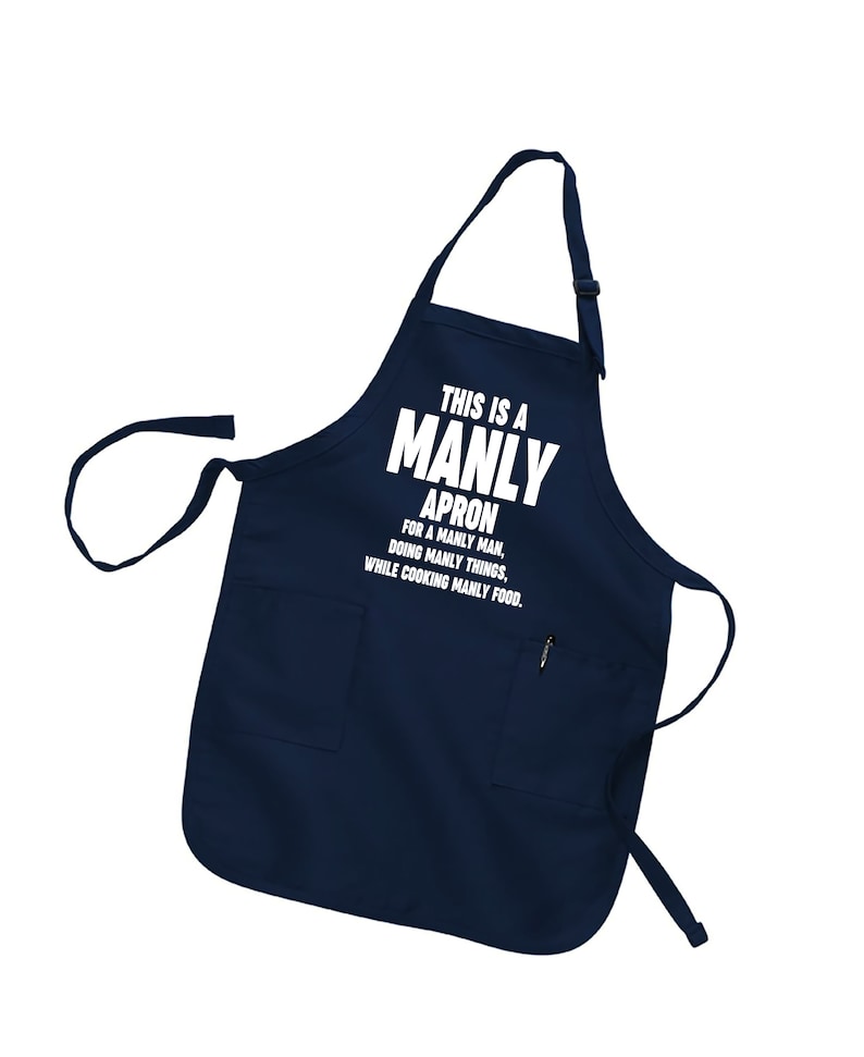 Puede incluir: Un delantal azul marino con un bolsillo blanco y el texto "THIS IS A MANLY APRON FOR A MANLY MAN, DOING MANLY THINGS, WHILE COOKING MANLY FOOD."