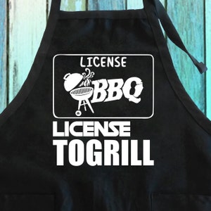 May include: Black apron with white text that reads "License BBQ License To Grill" and a graphic of a grill with smoke coming out of it.