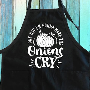 May include: Black kitchen apron with a white design that says "One day I'm gonna make the onions cry". The design also includes two white onions.