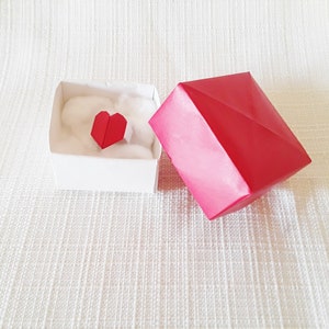 May include: A white box with a red origami heart inside, and a red origami box lid next to it.