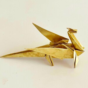 May include: A gold origami dragon with wings outstretched. The dragon is made of paper and has a detailed design.