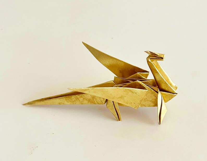May include: A gold origami dragon with wings outstretched. The dragon is made of paper and has a detailed design.