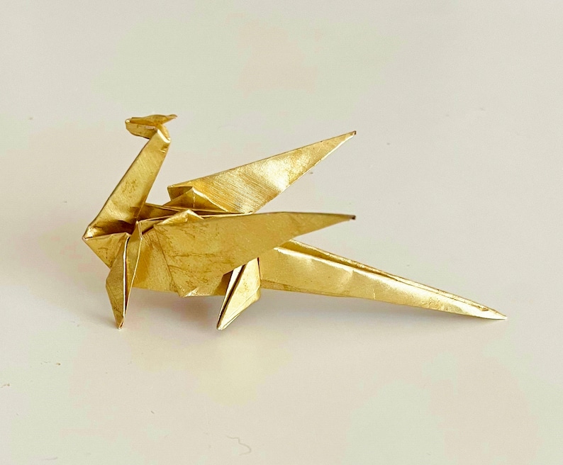 May include: A gold origami dragon with wings outstretched. The dragon is made of paper and has a detailed design.
