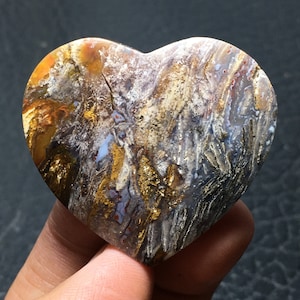 May include: A heart-shaped polished agate stone with a unique pattern of brown, gold, white, and blue colors. The stone has a smooth, polished surface and is perfect for jewelry making or as a decorative piece.