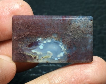 May include: A rectangular, polished agate cabochon with a brown, red, and white color pattern. The agate has a circular, white, and blue center with white dots.
