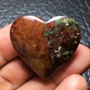 May include: A polished heart-shaped stone with a mix of colors. The stone features a blend of brown, green, and red hues. The heart is smooth and appears to be made of a natural material, possibly a gemstone or mineral.
