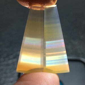 Puede incluir: Dos piezas de ágata iridiscente, cada una con un patrón diferente de bandas de color. La ágata es translúcida y tiene un color amarillo claro.