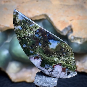 May include: A green, white and brown agate cabochon with a unique, swirling pattern. The cabochon is cut in a teardrop shape and has a polished finish.