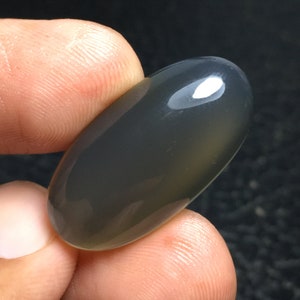 May include: A smooth, oval-shaped, gray agate cabochon with a polished finish.