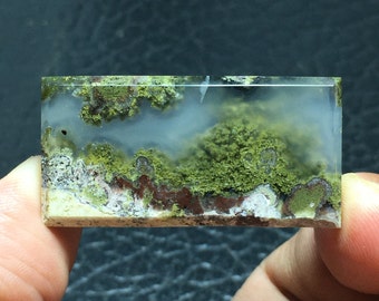 May include: A translucent green, white, and brown agate cabochon with a mossy pattern. The agate is cut into a rectangular shape and has a polished finish.