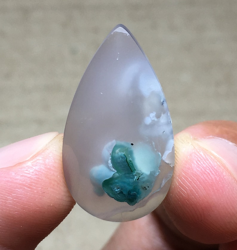 Peut inclure: Un cabochon d'agate en forme de larme avec une base blanche translucide et une inclusion verte et blanche au centre.