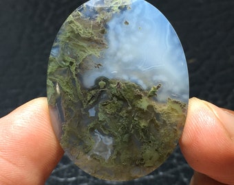 May include: Oval shaped agate cabochon with a white and green moss agate pattern. The stone has a translucent appearance with a light blue hue.