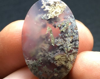 May include: A translucent oval cabochon gemstone with a pink base and intricate patterns of gray, green, and gold dendrites. The stone has a natural, organic look.