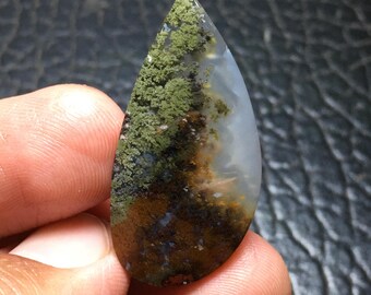 May include: A teardrop-shaped gemstone with a natural landscape pattern. The stone features a mix of green, brown, and white hues, resembling a miniature forest or mountain scene. The polished surface of the stone is smooth and reflective.