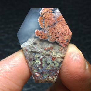 Peut inclure: Un cabochon d'agate hexagonal facetté et transparent avec un motif dendritique d'inclusions rouges, brunes et vertes.