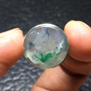 May include: A silver ring with a round, clear stone featuring green, white, and black swirls.