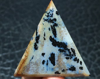 Könnte beinhalten: Eine dreieckige, polierte, weiße Achatpyramide mit schwarzen und goldenen Einschlüssen. Die Pyramide ist etwa 5 cm hoch.