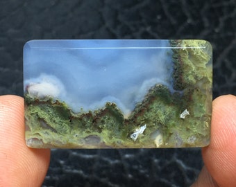 May include: A rectangular, light blue agate cabochon with green and brown dendritic patterns. The agate has a cloudy, sky-like appearance.
