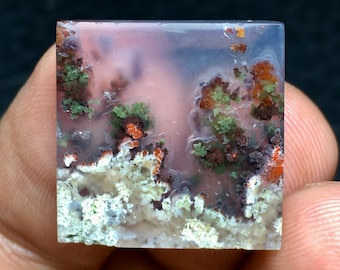 Könnte beinhalten: Ein quadratischer, durchscheinender, hellrosafarbener Achat-Cabochon mit braunen, grünen und weißen dendritischen Mustern.