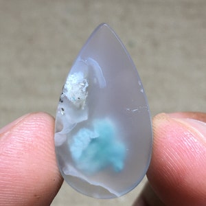 Peut inclure: Un cabochon d'agate en forme de larme avec un motif translucide blanc et bleu. L'agate a un aspect nuageux, laiteux avec un centre bleu-vert.
