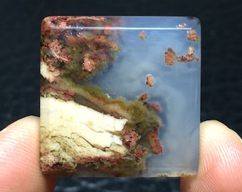 Könnte beinhalten: Ein quadratischer, durchscheinender, hellblauer Achat-Cabochon mit braunen, weißen und roten Einschlüssen. Der Achat hat ein geschichtetes, gebändertes Muster.