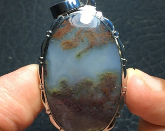 May include: A silver pendant with an oval-shaped agate stone. The stone has a cloudy white background with brown and green patterns.