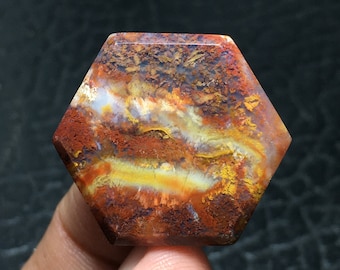 Könnte beinhalten: Ein sechseckiger, polierter Achat-Edelstein mit einem wirbelnden Muster aus Rot, Orange, Gelb und Weiß. Der Achat hat eine natürliche, raue Textur.
