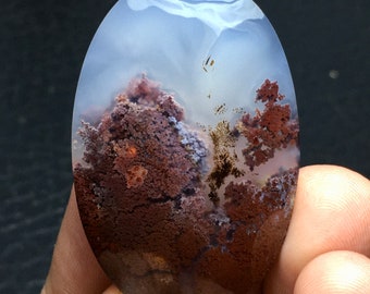 May include: A polished agate cabochon with a unique pattern of brown, purple, and white. The agate has a cloudy, translucent appearance with a variety of textures.