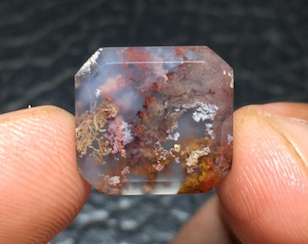 Può includere: Una pietra preziosa traslucida e sfaccettata con un motivo unico e vorticoso di marrone, bianco e rosa. La pietra ha un aspetto naturale e organico.