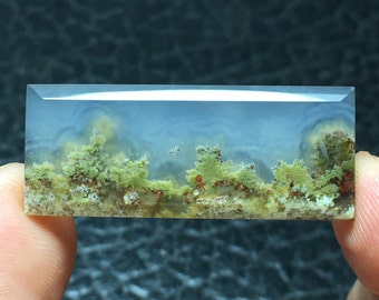 May include: A translucent, light blue agate cabochon with a landscape pattern of green and red dendrites. The agate has a polished, smooth surface.