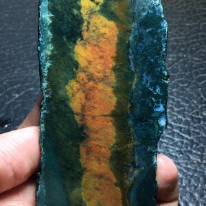 May include: A slab of polished green, yellow, and orange agate with a rough edge. The agate has a unique pattern of swirling colors.
