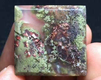 May include: A square, green, brown, and white agate cabochon with a polished surface. The stone has a unique, natural pattern of swirls and inclusions.