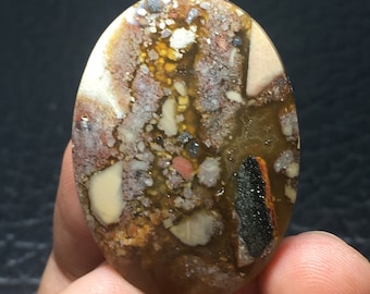 May include: An oval cabochon gemstone with a speckled pattern in shades of brown, white, black and red. The stone has a variety of colours and textures.