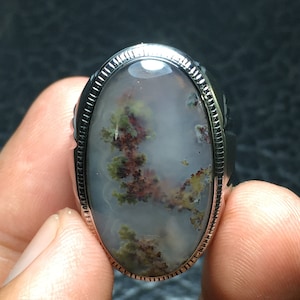 Könnte beinhalten: Ein silberner Ring mit einem ovalen Achat-Stein. Der Stein hat einen weißen Hintergrund mit braunen und grünen Mustern.