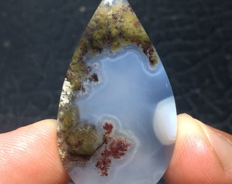 Könnte beinhalten: Ein tropfenförmiger Achat-Cabochon mit einer weißen, blauen und grünen Basis und roten und braunen dendritischen Mustern.