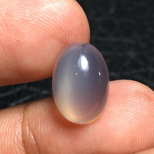 May include: A smooth, oval-shaped, light gray gemstone with a subtle shimmer.