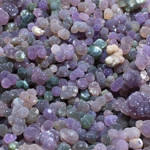 Puede incluir: Primer plano de una colección de piedras de ágata púrpura y verde. Las piedras son lisas y redondas, y tienen una variedad de tamaños y formas.