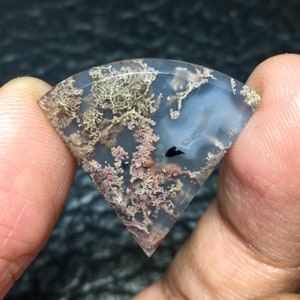 May include: A translucent, agate cabochon with a dendritic pattern in shades of brown, pink, and white. The agate has a natural, organic look.