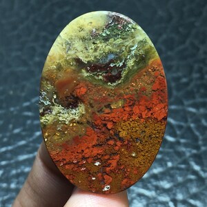 Könnte beinhalten: Ein bunter Achat-Cabochon mit einer Mischung aus roten, orangen, gelben und grünen Farben. Der Stein hat ein einzigartiges Muster und ist perfekt für die Schmuckherstellung.