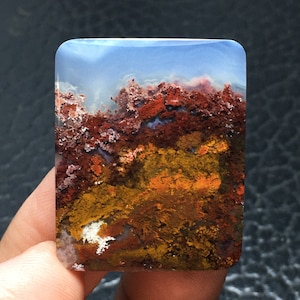 May include: A polished agate stone with a layered pattern of red, orange, and yellow. The stone has a smooth, polished surface and a translucent appearance.