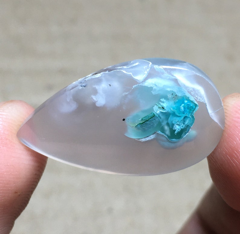 Peut inclure: Un cabochon en agate transparente en forme de larme avec un amas de cristaux bleu-vert &agrave; l'int&eacute;rieur.