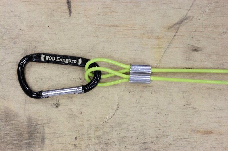 May include: A black carabiner with the text "WOD Hangers" on it is attached to two lime green ropes with silver metal sleeves.