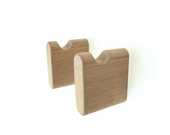 May include: Two wooden wall hooks with a rounded top and a cutout in the center. The hooks are made of light brown wood and have a natural finish.