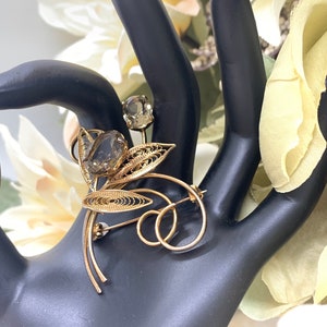 May include: A gold filigree brooch with two brown faceted stones. The brooch is shaped like a flower with delicate leaves.